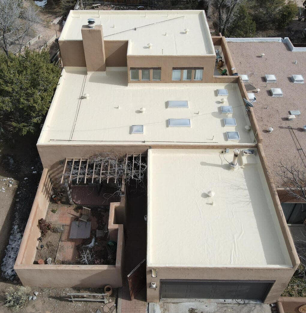 Drone image of a multi-sectioned, multi-storied flat roof system in Albuquerque, New Mexico, coated with tan silicone, featuring skylights for natural lighting.