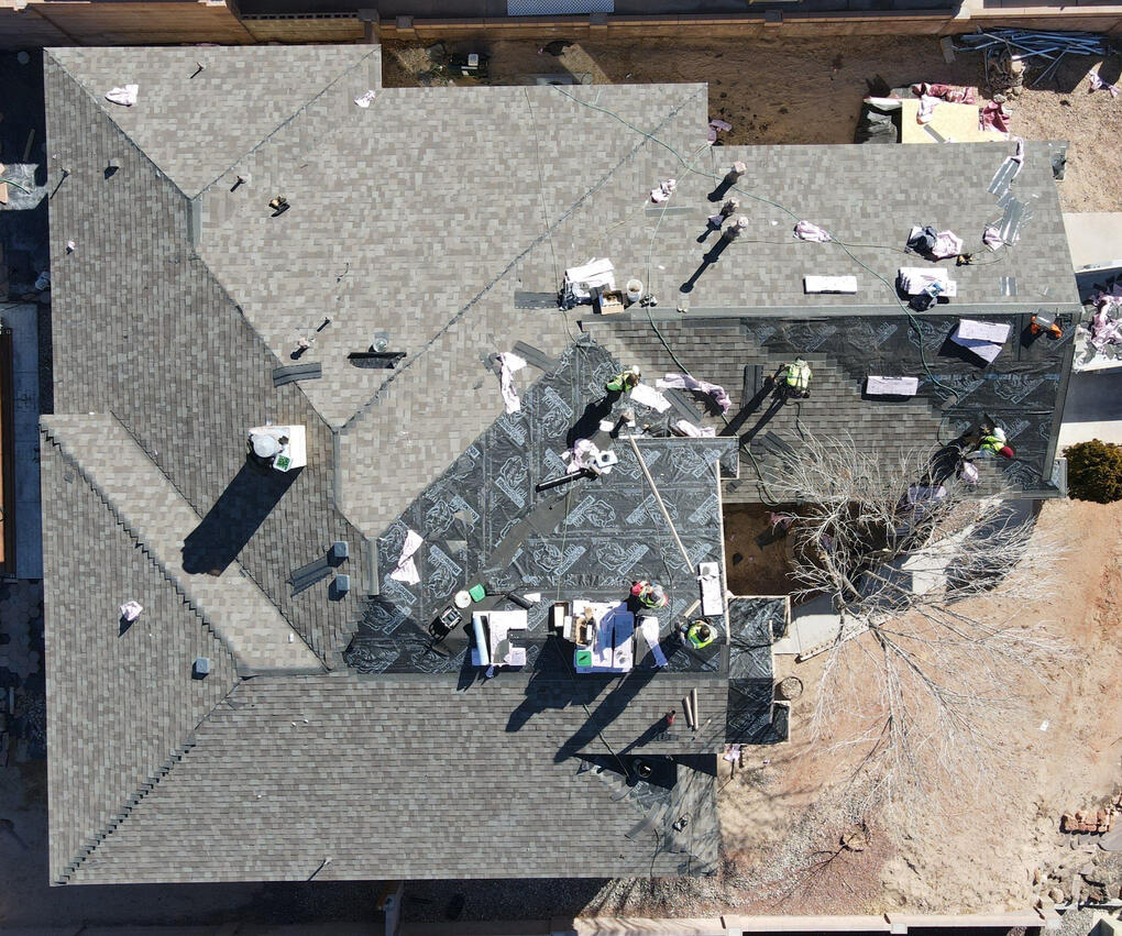 Drone image from above of a residential roof in Albuquerque, New Mexico, almost complete with the installation of grey shingles. Multiple roofers are actively working on the site.
