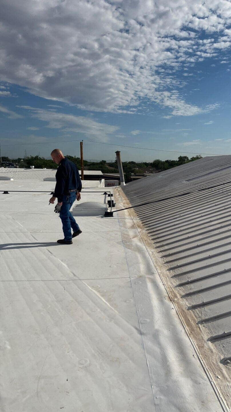 A project manager walking on a commercial flat white TPO roof in Albuquerque, New Mexico, inspecting the ongoing project.
