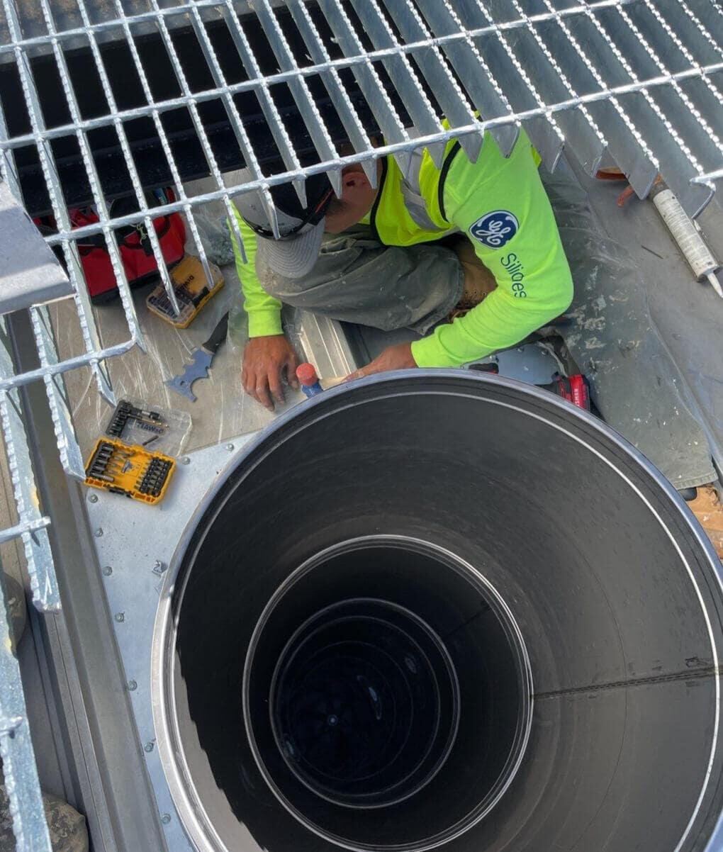 A roofer working on a commercial roof in Albuquerque, New Mexico, installing a large industrial vent.