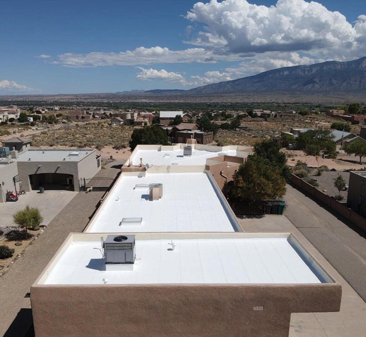 Drone view of a residential home with a flat roof in Rio Rancho, New Mexico, coated in white silicone, showcasing the reflective and protective finish.