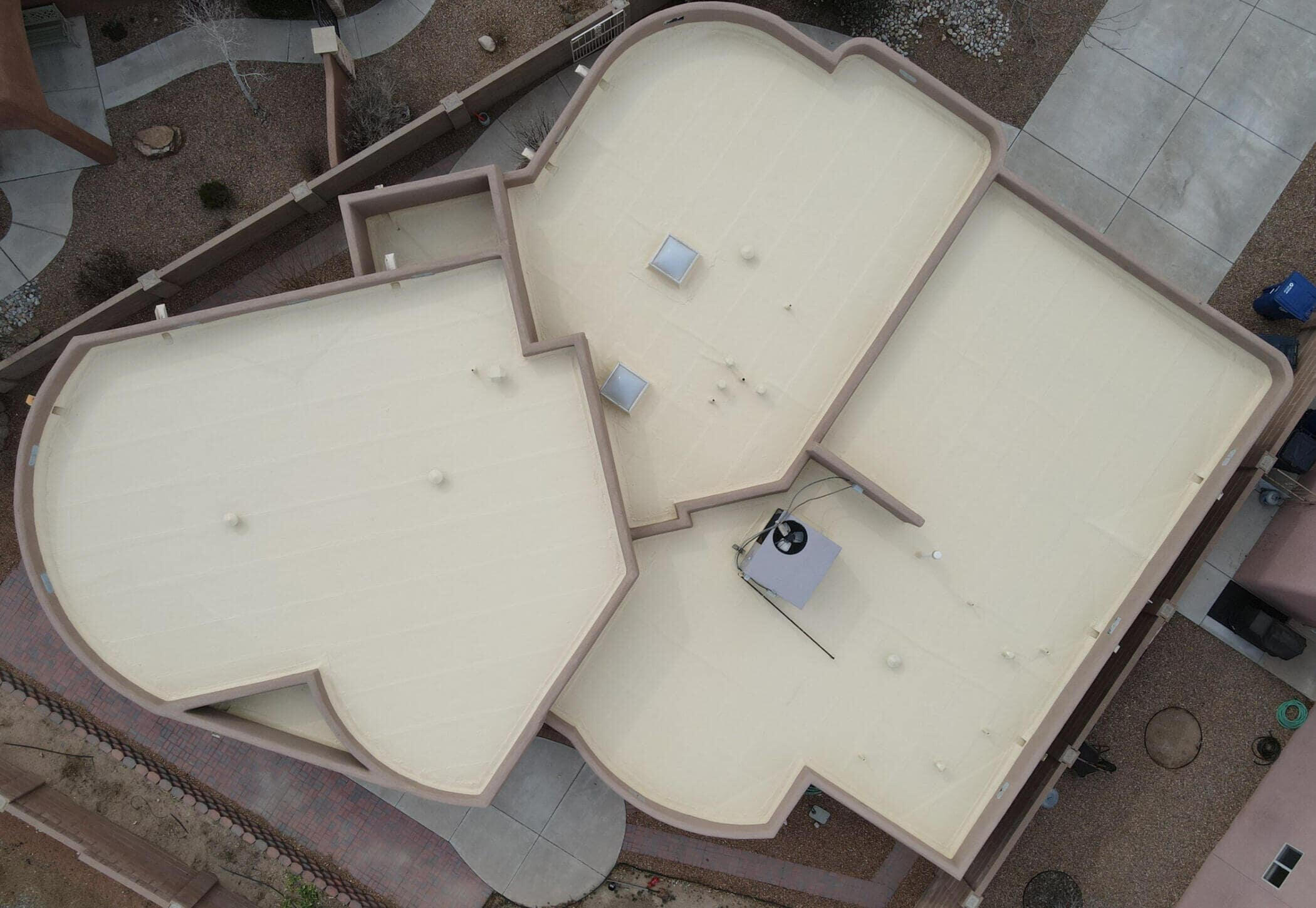 Drone shot from above showcasing a newly applied tan silicone roof coating on a flat residential roof in Albuquerque, featuring skylights.