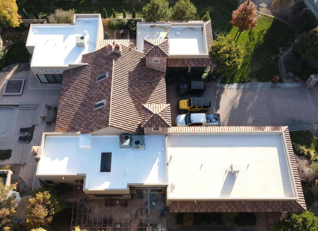Drone overhead view of a residential roof in Albuquerque, New Mexico, featuring flat sections covered in Thermoplastic Polyolefin (TPO) and pitched sections with a tile roofing system.