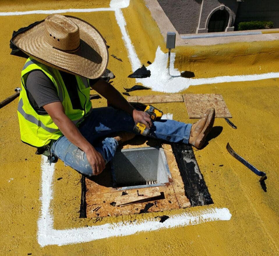 Roofer in Albuquerque, New Mexico, actively repairing a leaking vent on a flat roof, demonstrating skilled repair and maintenance work.