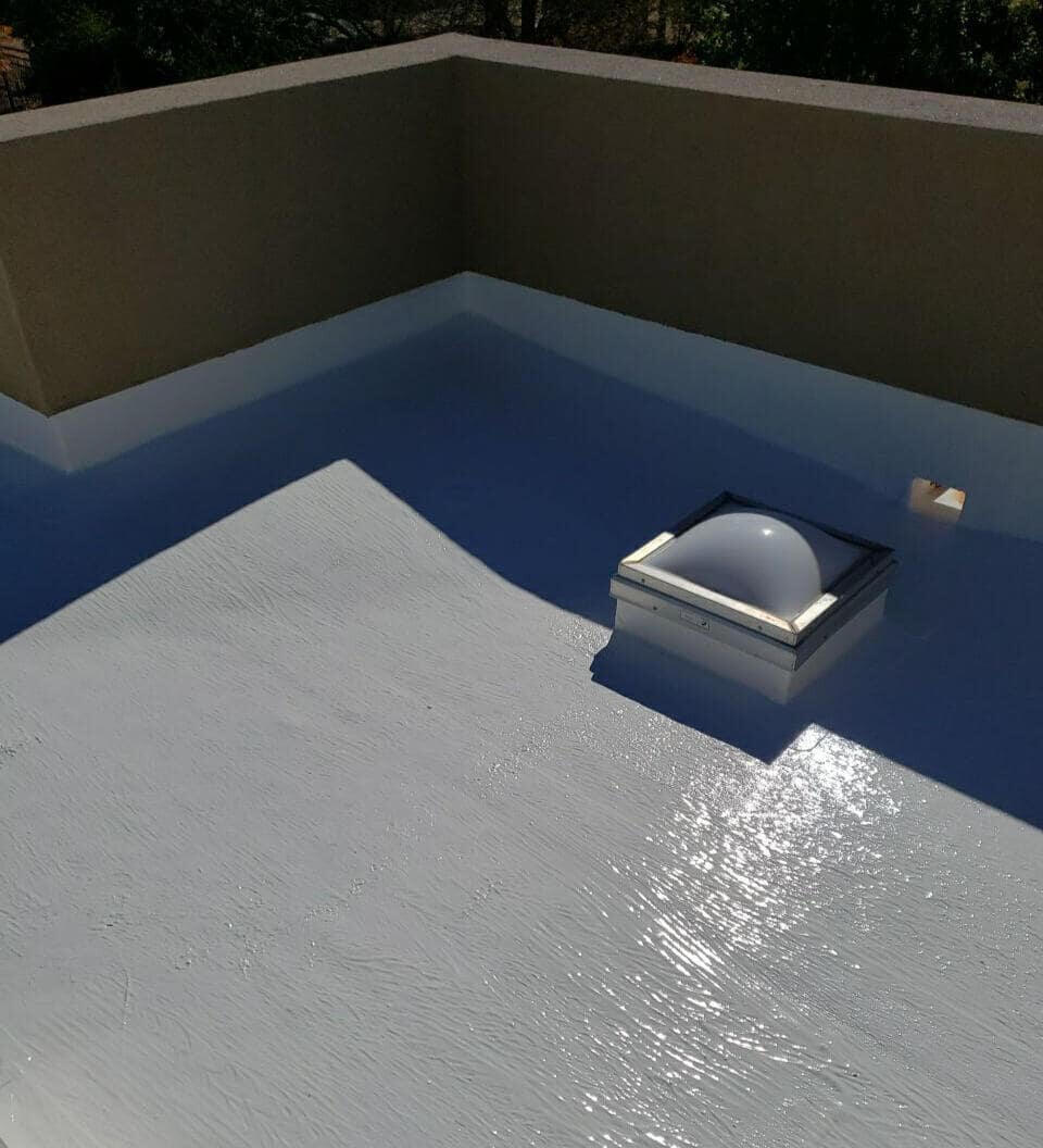 Silicone coating patch applied over a flat roof system in Albuquerque, New Mexico, to repair a customer's leak. The section includes a skylight and a water scupper for drainage.