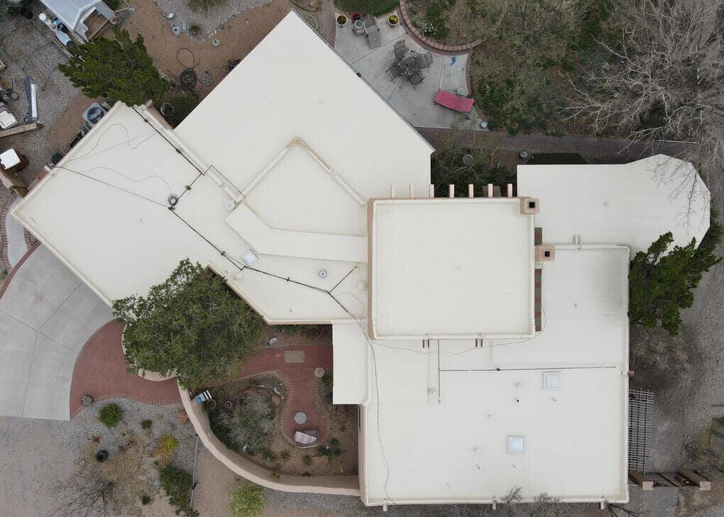 Drone view from above of a large residential home in Albuquerque, New Mexico, with a tan silicone coating applied to the flat roof system to repair leaks in the existing roof.