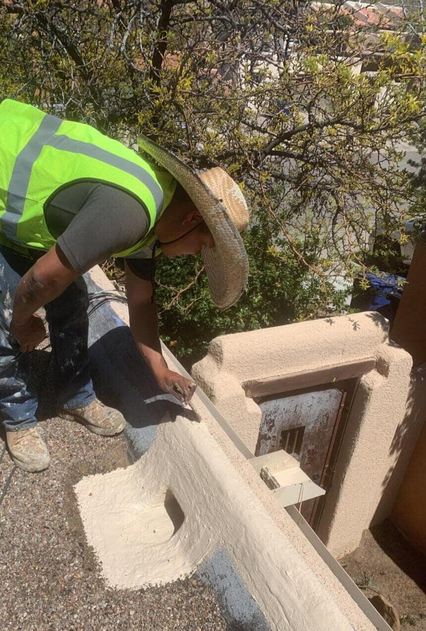 Roofer performing maintenance on a flat roof in Albuquerque, New Mexico, fixing a scupper on a parapet wall using tan silicone mastic.