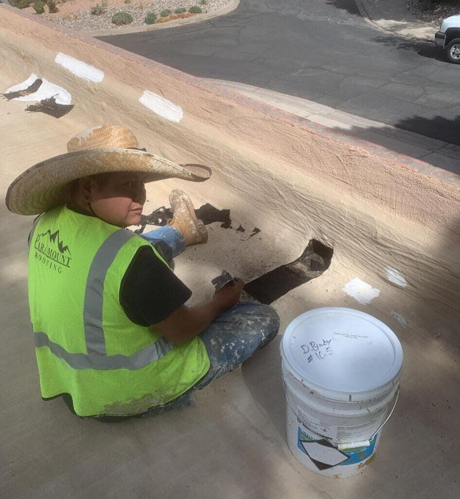 Roofer working on a flat roof in Albuquerque, New Mexico, maintaining a scupper using silicone mastic to ensure proper water drainage off the roof.