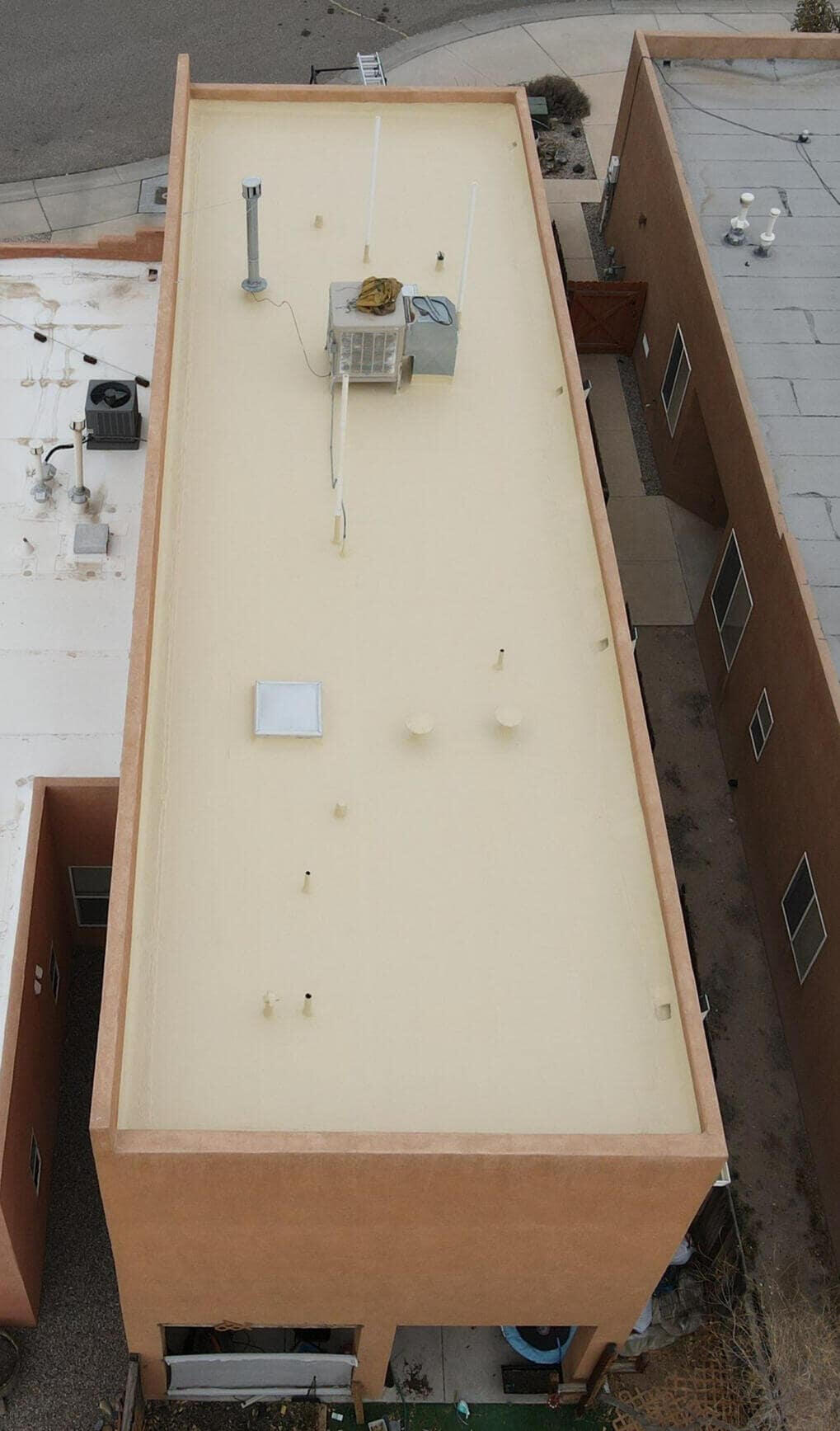 Drone view from above of a two-storey residential home in Albuquerque, New Mexico, with a well-maintained tan silicone coating on the flat roof system, featuring skylights.