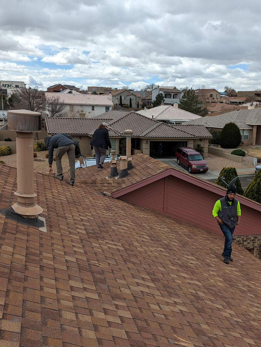 Two insurance adjusters and a Paramount Roofing project manager on a pitched shingle roof in Albuquerque, New Mexico, inspecting the roof for a wind damage insurance claim.