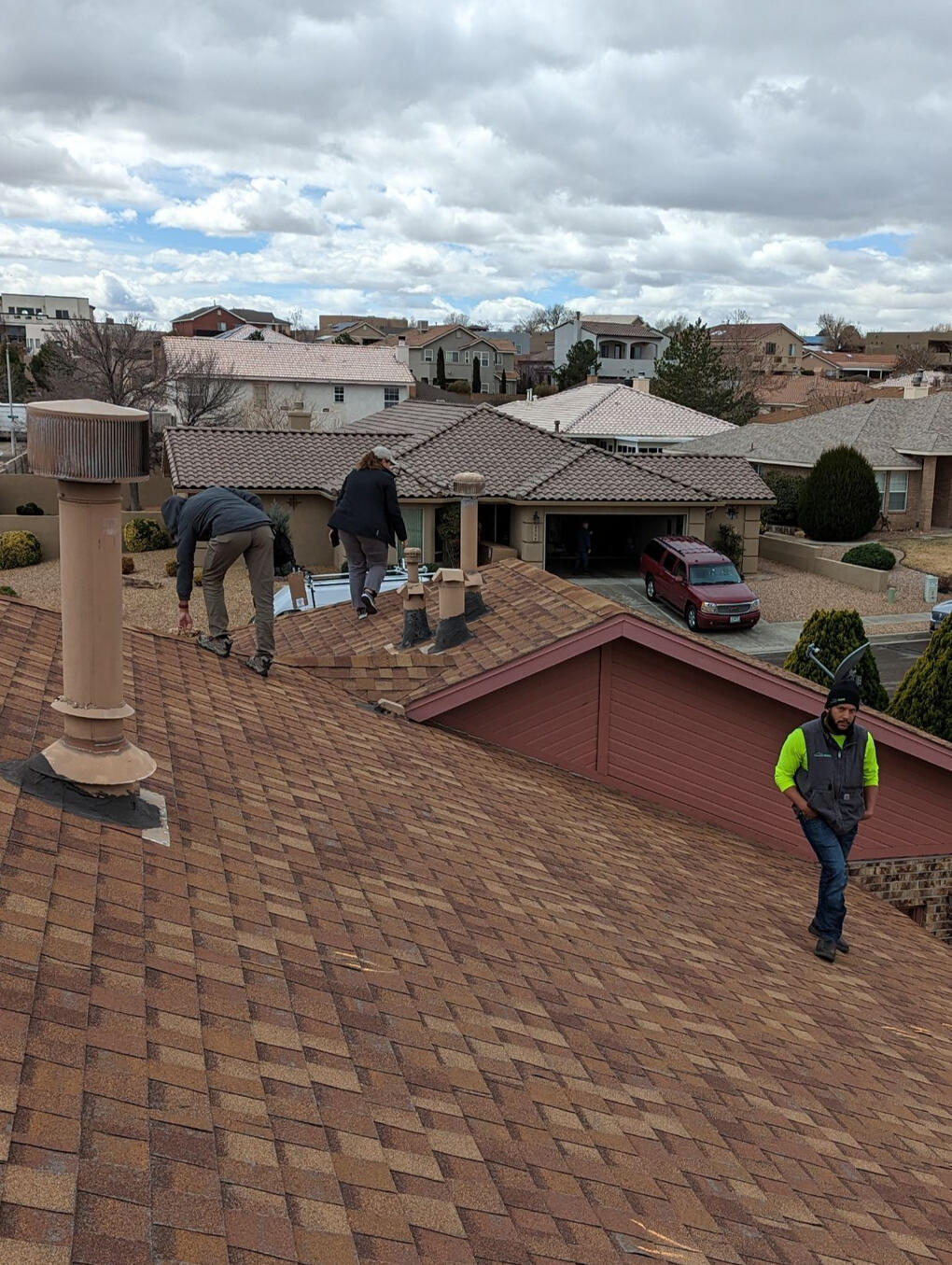 Two insurance adjusters and a Paramount Roofing project manager on a pitched shingle roof in Albuquerque, New Mexico, inspecting the roof for a wind damage insurance claim.
