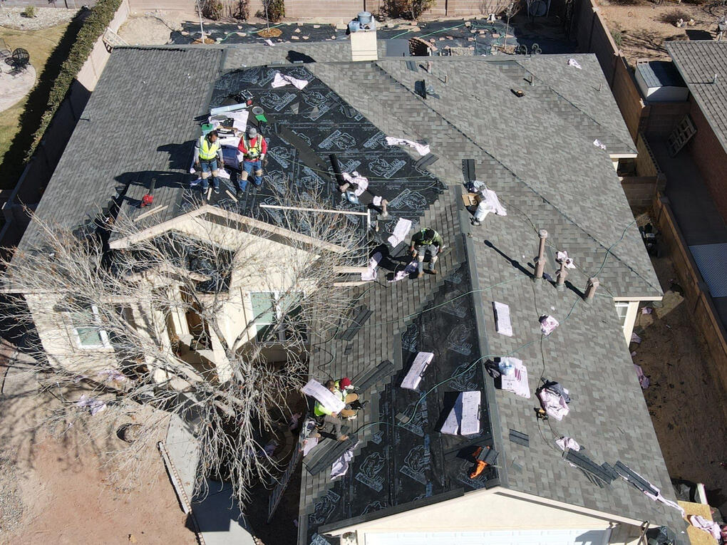 Drone image from above of a residential roof in Albuquerque, New Mexico, almost complete with the installation of grey shingles. Multiple roofers are actively working on the site.